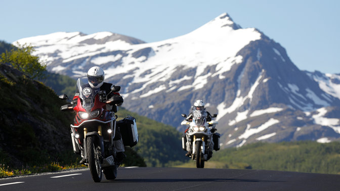 Twee motoren rijdend op de weg met besneeuwde bergen in de verte.