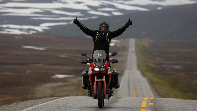 Man on a Honda Africa Twin with his arms raised high on the roads in Nordkapp.