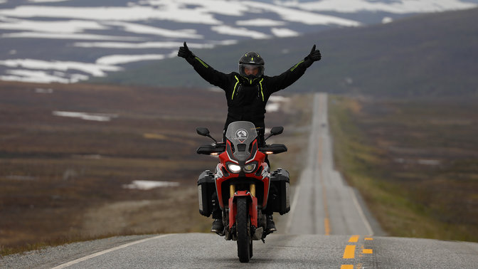 Um homem numa Honda Africa Twin com os braços no ar nas estradas em Nordkapp.