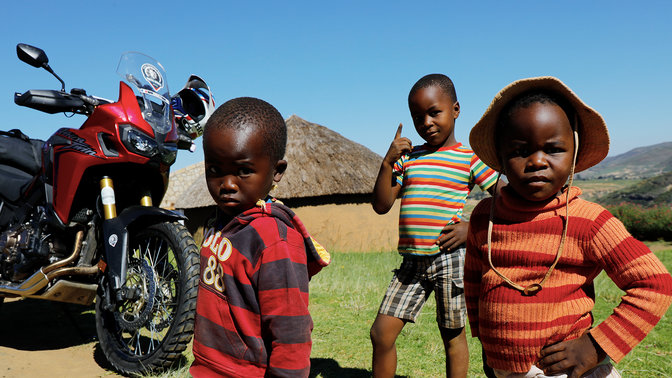 De jeunes enfants à l'extérieur rassemblés autour d'un Africa Twin CRF1000L.