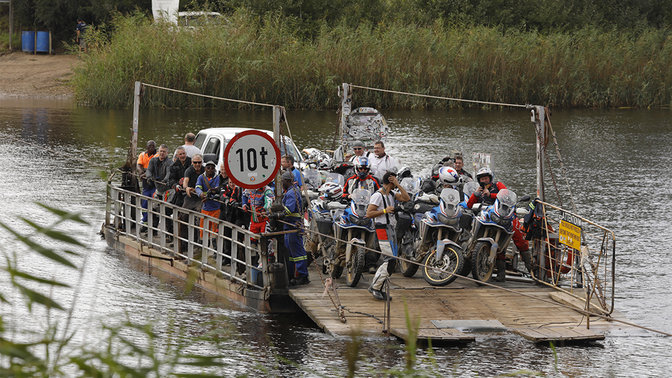 Motorrad, das auf einem Boot über einen Fluss transportiert wird.