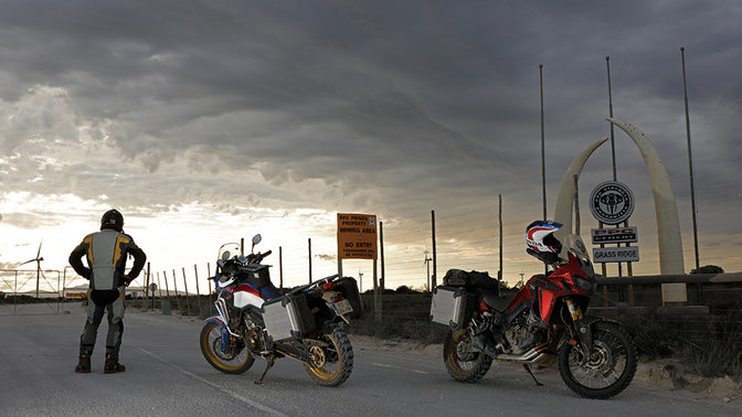 Piloto mirando hacia el horizonte junto a dos Africa Twin aparcadas en la calzada.