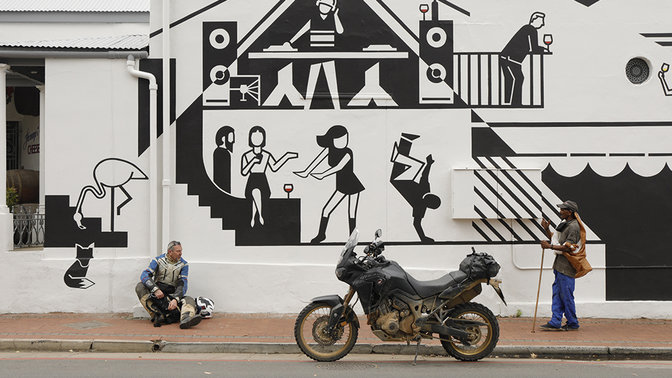 Jezdec se zaparkovaným motocyklem sedící u zdi pokryté street artem.