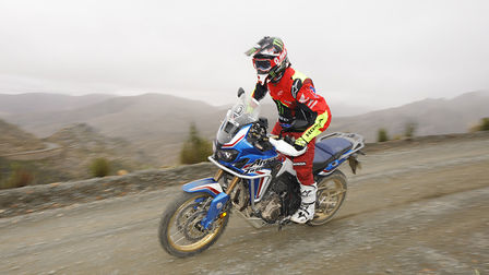 Boční pohled na motocykl Honda Africa Twin s jezdcem v přírodě.