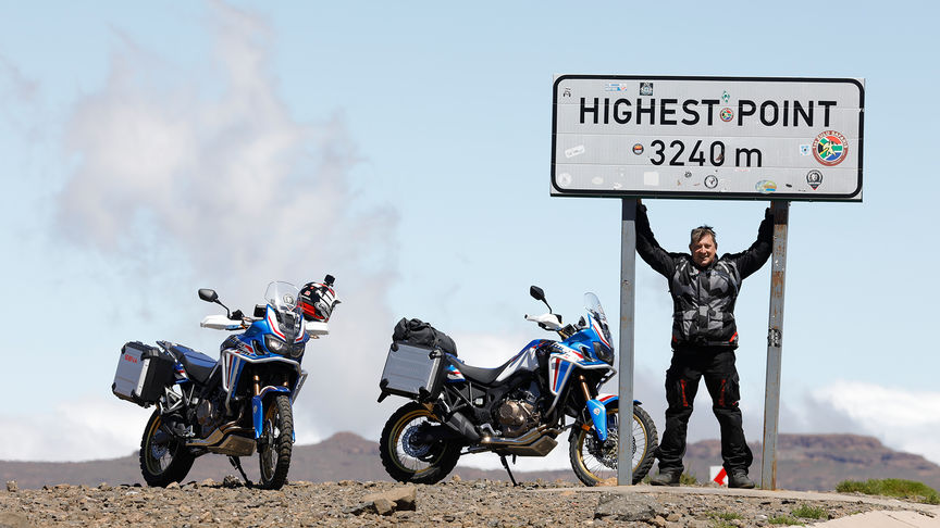 Pilota in piedi nel punto più meridionale del Sud Africa, accanto a due moto.