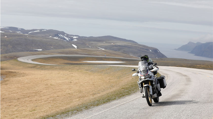 Pilota in piedi nel punto più meridionale del Sud Africa, accanto a due moto.