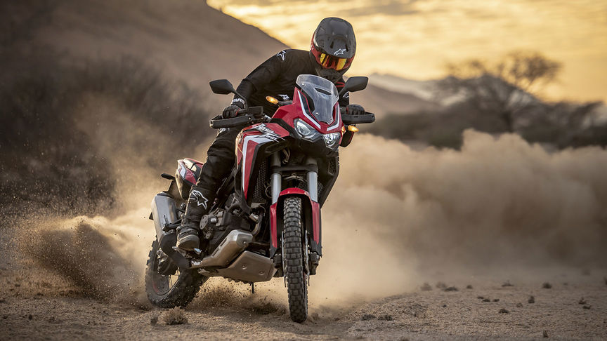 Pilota in piedi nel punto più meridionale del Sud Africa, accanto a due moto.